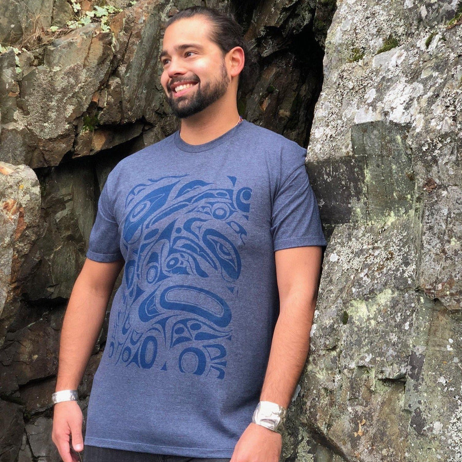 Model outside wearing unisex t-shirt raven and eagle motif by indigenous artist in blue