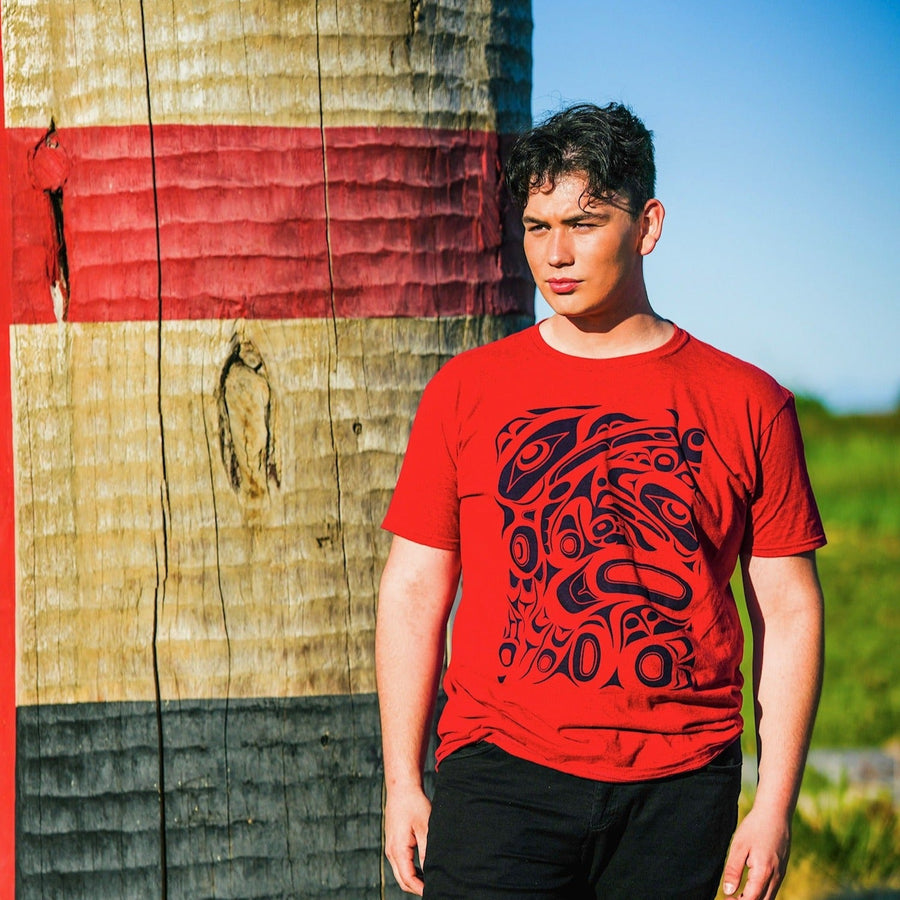 Model outside wearing unisex t-shirt raven and eagle motif by indigenous artist in red