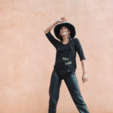 Model wearing womens organic cotton top by indigenous artist featuring hummingbirds wearing a hat