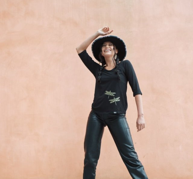 Model wearing womens organic cotton top by indigenous artist featuring hummingbirds wearing a hat