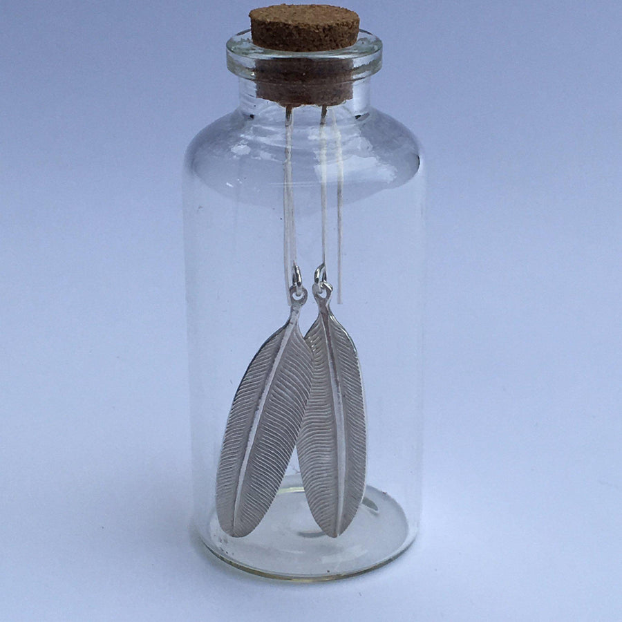 Close up of earrings silver feather by indigenous artist inside bottle